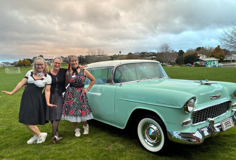 Three Rotary Club of Omokoroa members beside a vintage Chevrolet at the Rock and Roll Bash.
